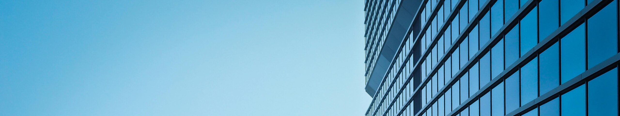 Low angle view of a modern skyscraper with reflective glass facade and blue sky.