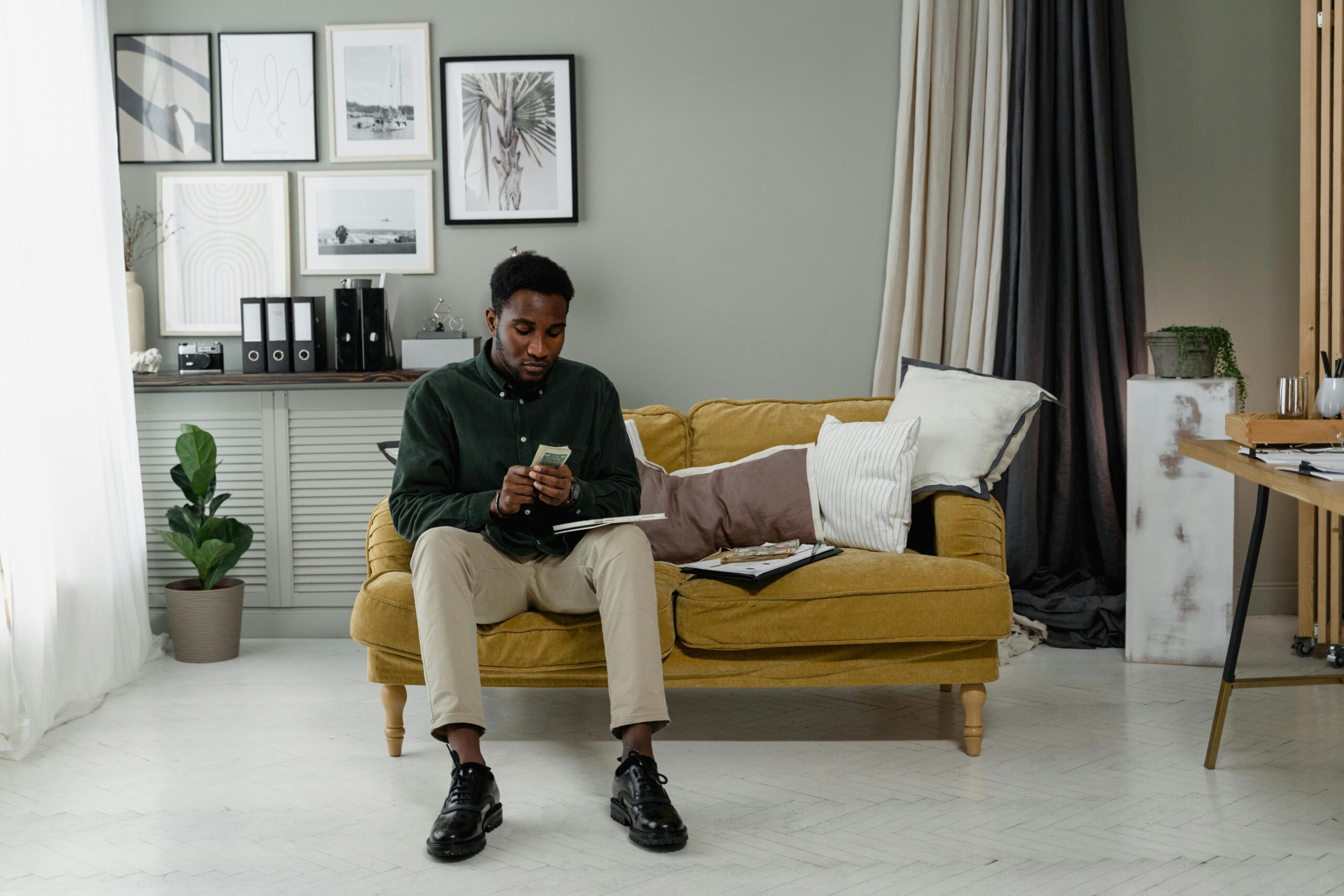 Professional man counting cash, seated on a sofa in a modern and minimalist home office setting.