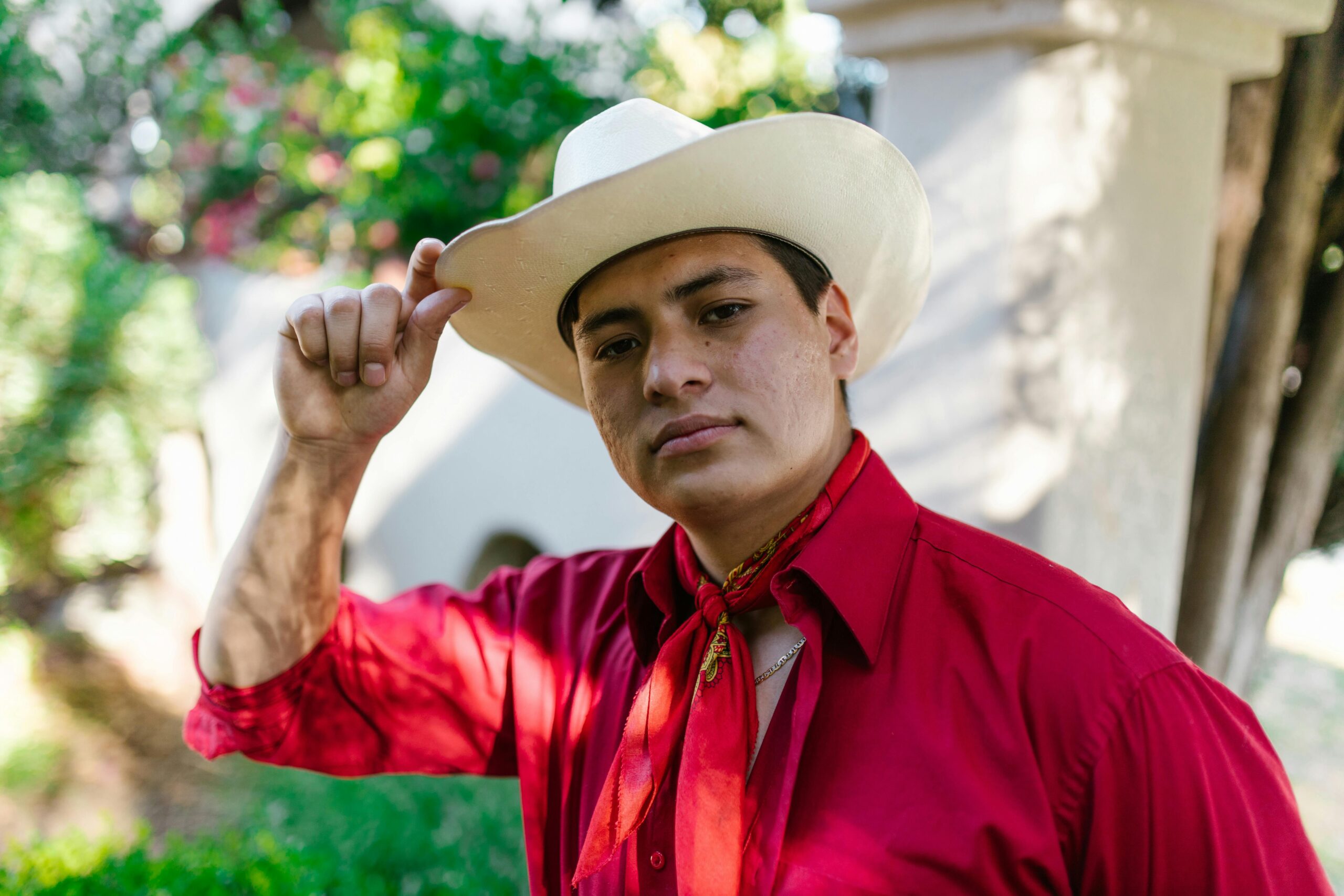 Young Hispanic man in traditional Mexican attire with a white hat and red shirt outdoors.